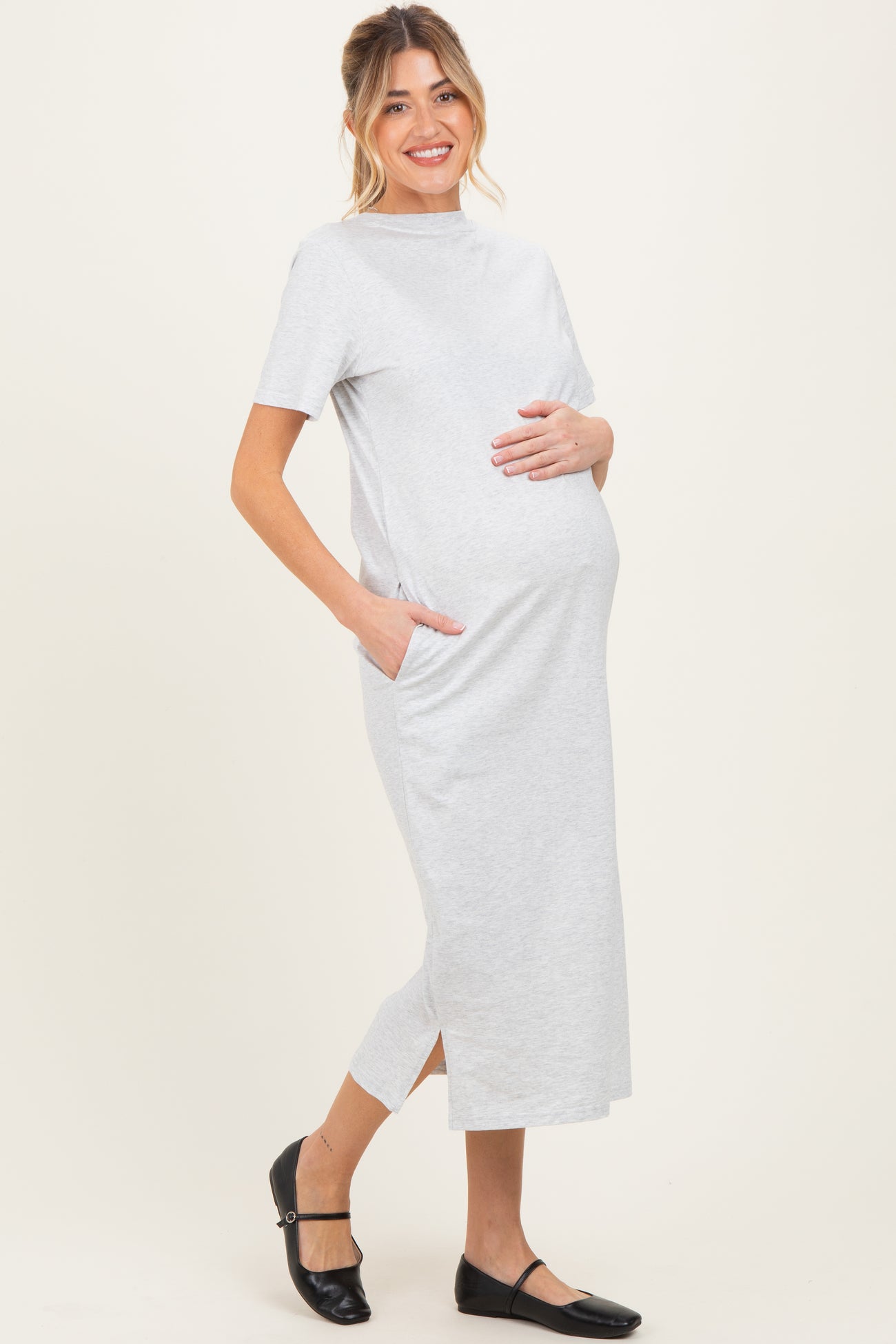 woman wearing a grey short sleeve maternity dress with pockets and side slit, holding her baby bump
