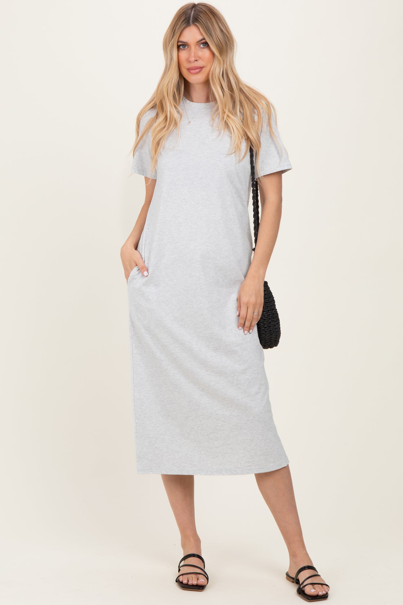 woman wearing a grey short sleeve maxi dress with pockets and holding a black woven bag