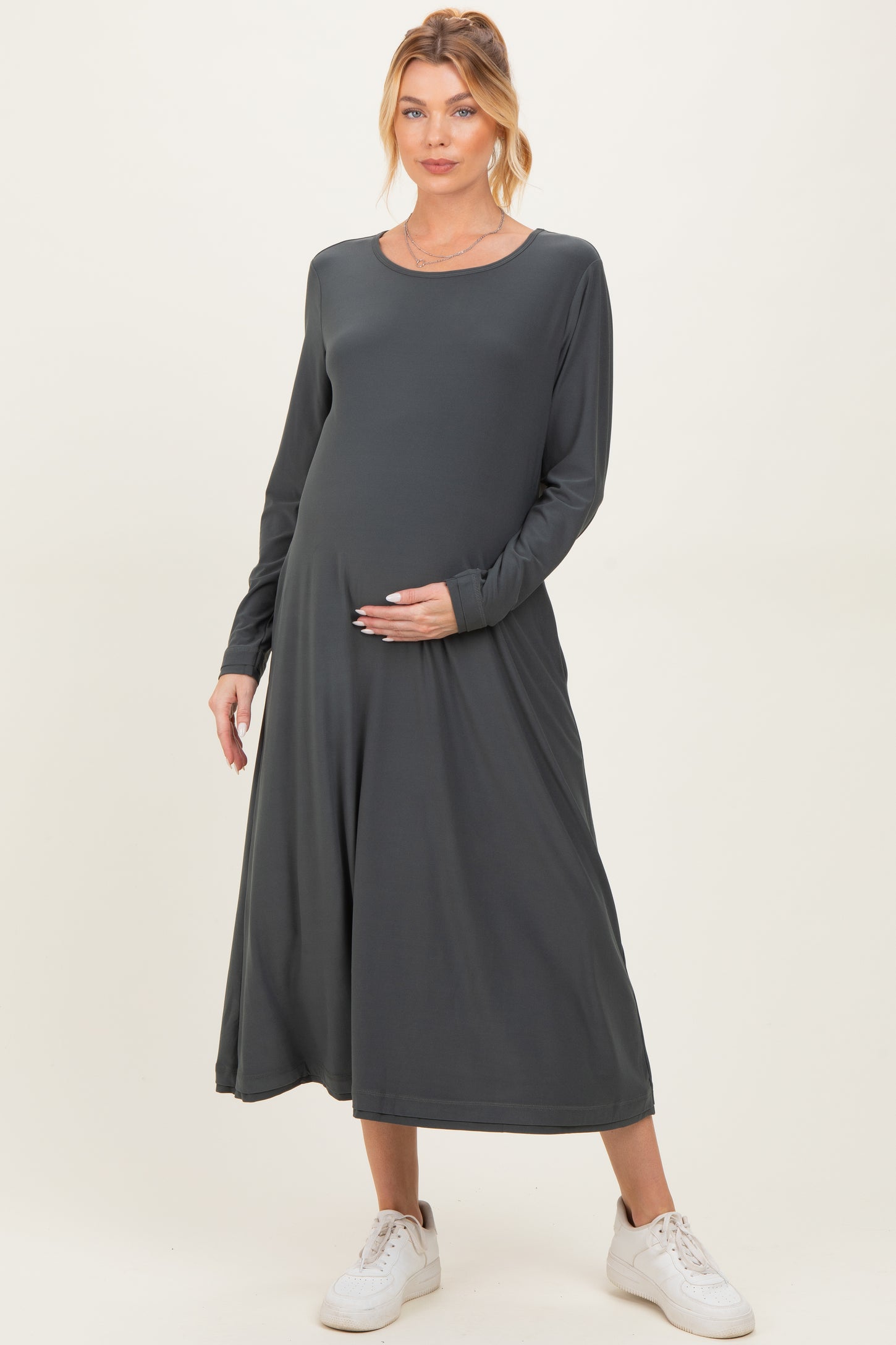 woman wearing a dark gray long sleeve maternity dress, gently cradling her baby bump