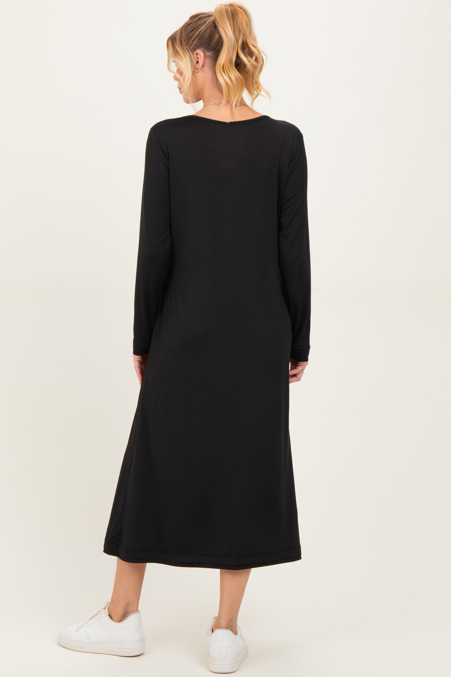 woman wearing a black long sleeve maternity dress, showing the back view, paired with white sneakers