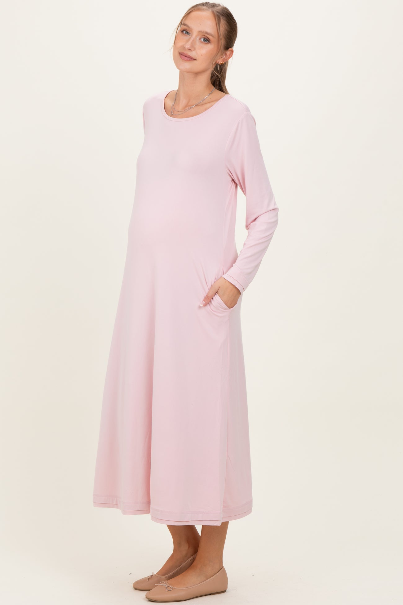 woman wearing a light pink long sleeve maternity dress with pockets and a visible baby bump