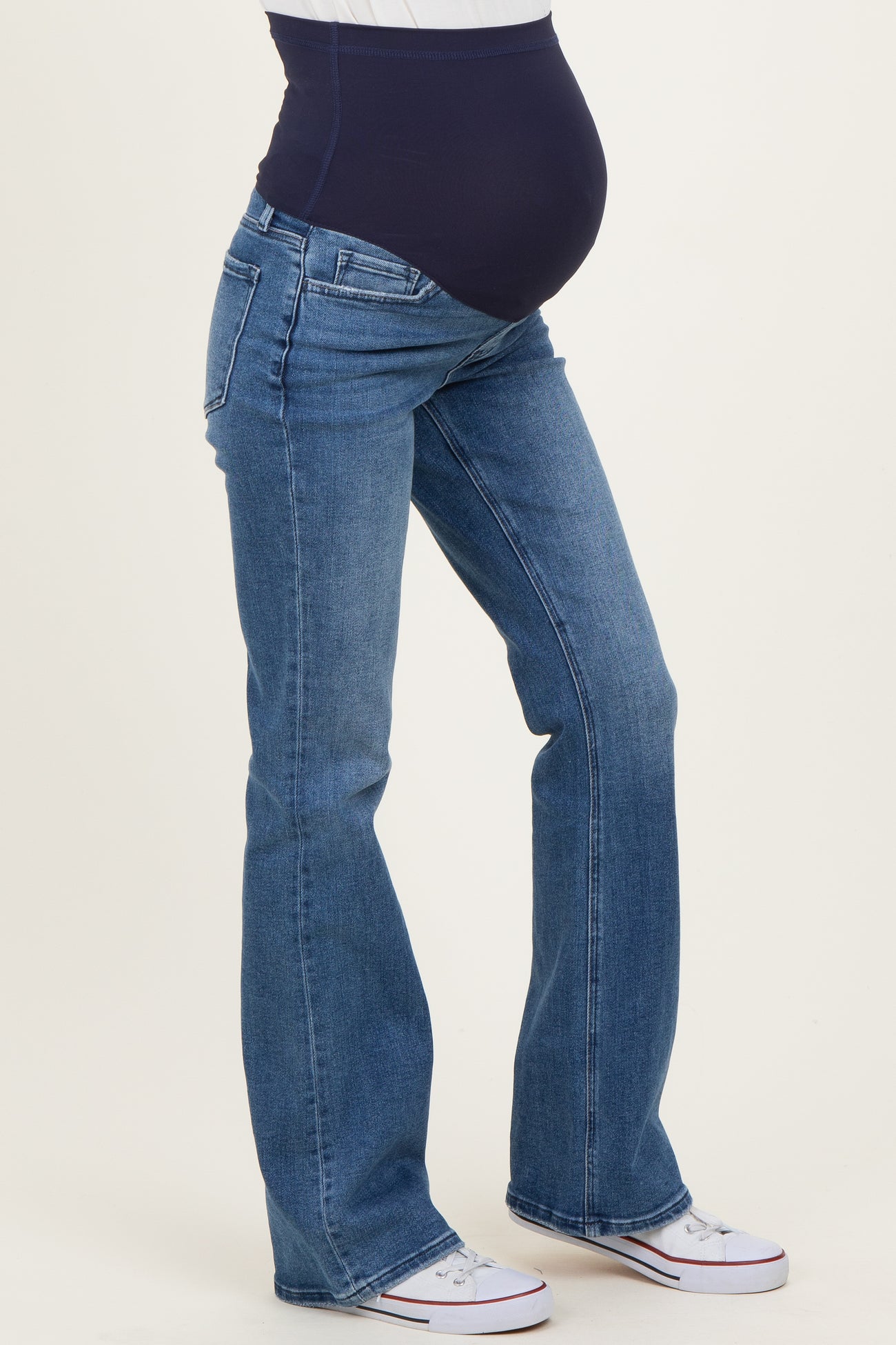 woman wearing dark blue belly panel maternity jeans with a fitted waist and flared legs, showcasing her baby bump