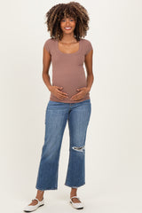 woman wearing a brown maternity ribbed scoop neck top and holding her baby bump, paired with distressed blue jeans