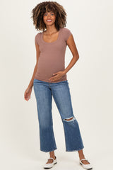 woman wearing a mauve ribbed maternity top and blue flared jeans, gently holding her baby bump