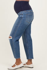 woman wearing blue maternity jeans with a visible baby bump and distressed details, styled with white flats