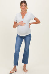 woman wearing a light gray maternity short sleeve top and blue flared jeans, holding her baby bump