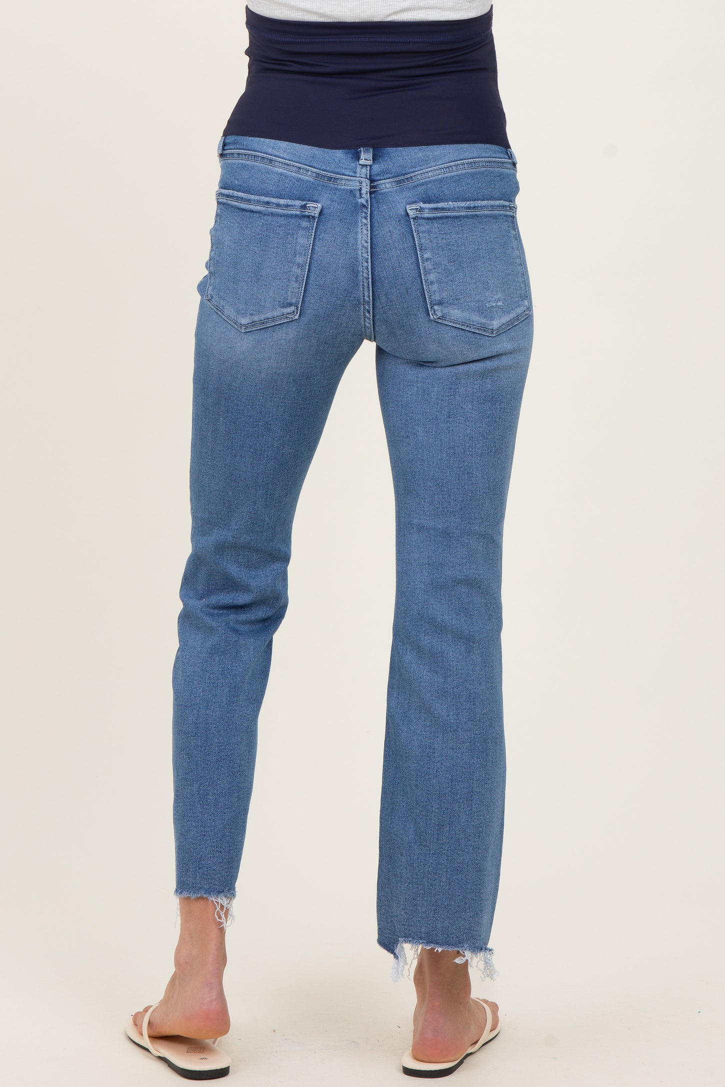 woman wearing light blue maternity jeans with a stretchy black waistband, showing frayed hem at the ankles
