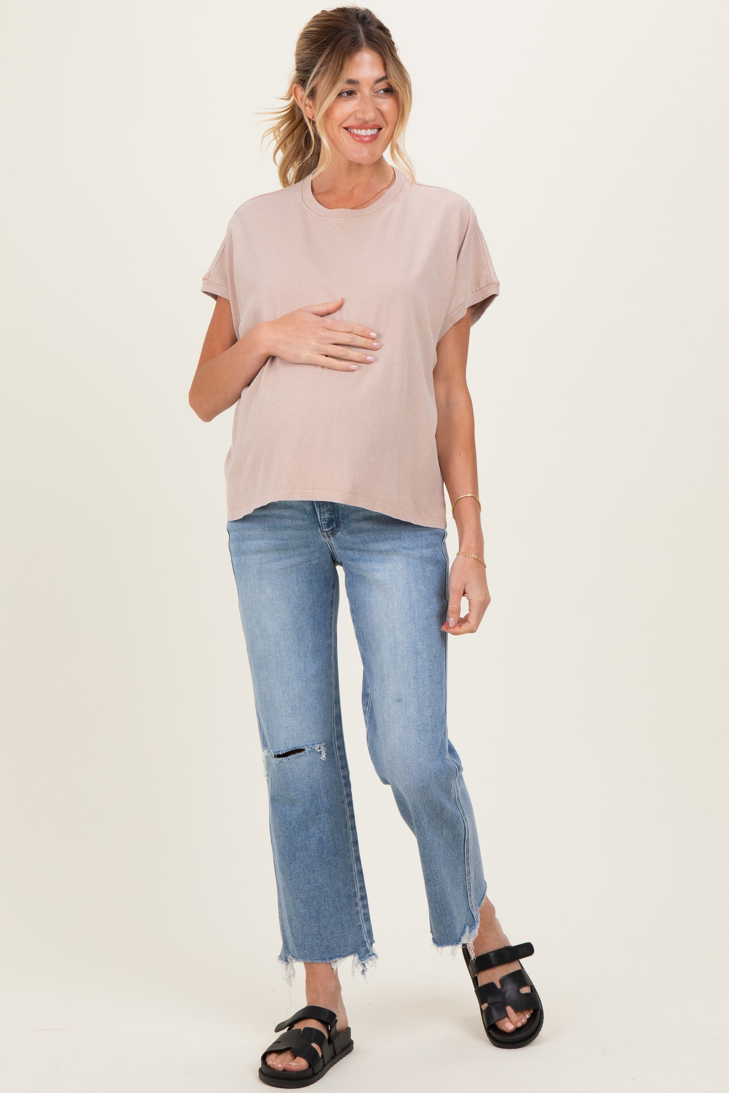 woman wearing a light pink maternity t-shirt and blue ripped jeans, holding her baby bump