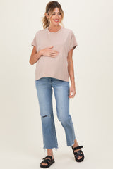 woman wearing a light pink maternity t-shirt and blue ripped jeans, holding her baby bump