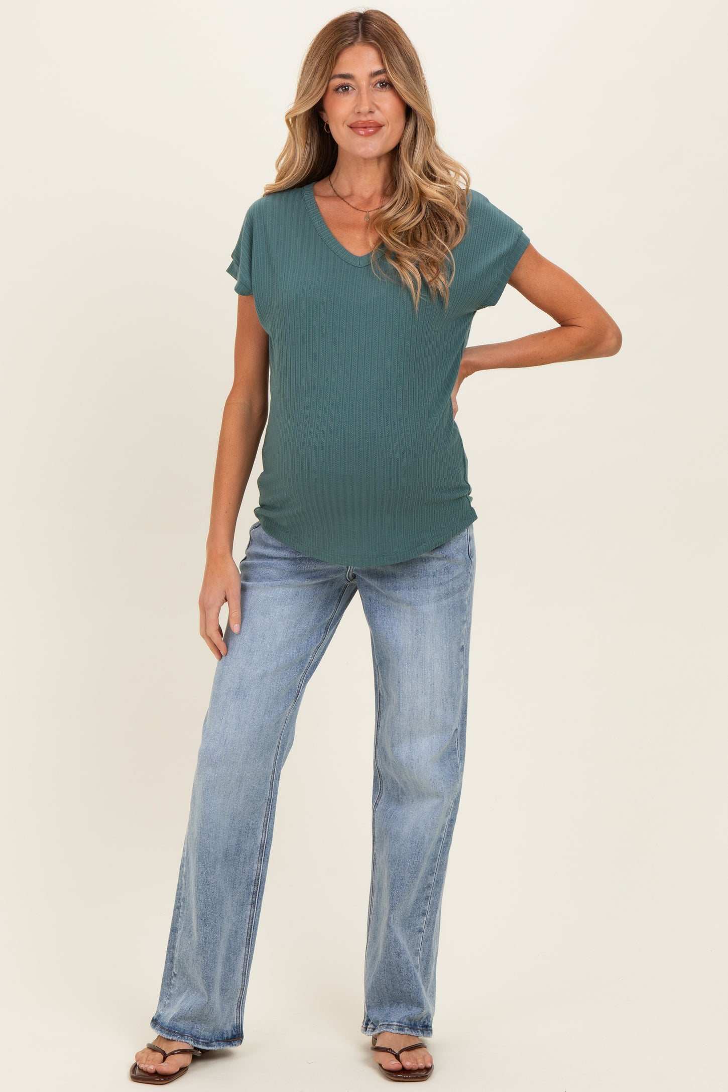 woman wearing a teal maternity top with short sleeves and a v-neck, paired with light blue flared jeans and showing a baby bump