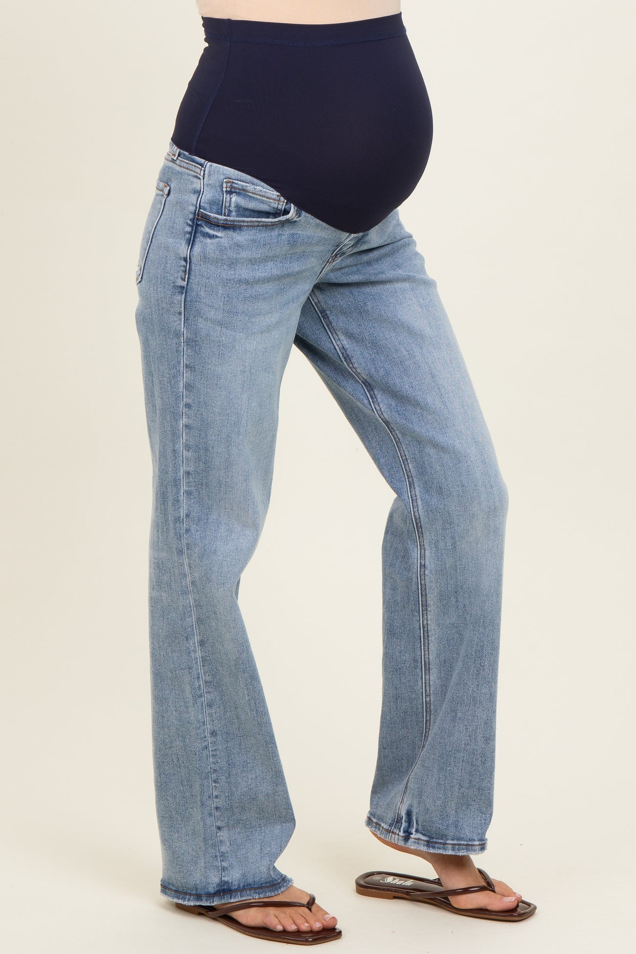 woman wearing a pair of light blue maternity jeans with a dark blue over-the-bump panel and standing with a visible baby bump