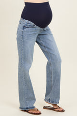 woman wearing a pair of light blue maternity jeans with a dark blue over-the-bump panel and standing with a visible baby bump