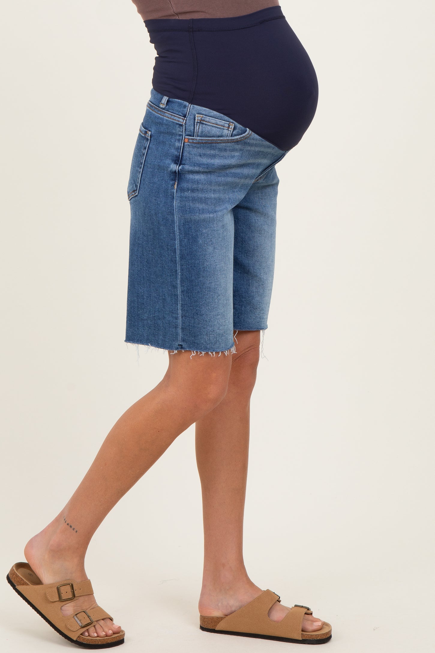 woman wearing maternity denim shorts with a blue panel and frayed hem, featuring a visible baby bump