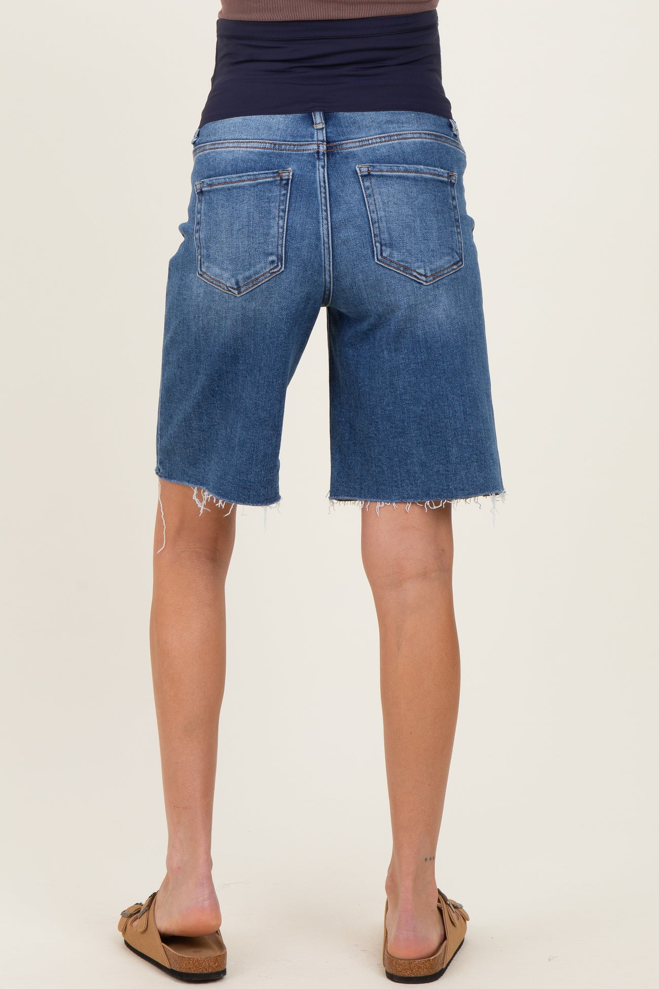 woman wearing maternity denim shorts in a mid-blue wash with frayed hems, viewed from the back