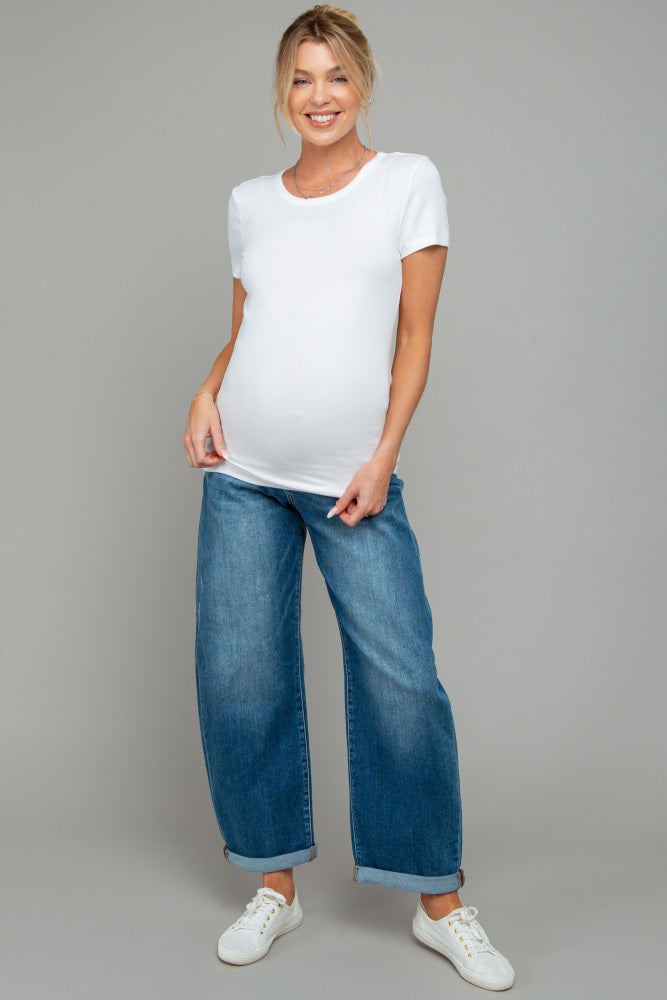 woman wearing a white short sleeve maternity top and blue wide-leg jeans, highlighting her baby bump