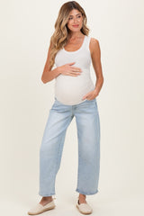 woman wearing a white ribbed tank top and light blue wide-leg maternity jeans, holding her baby bump