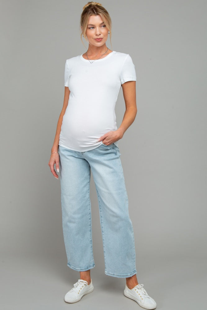 woman wearing a white short sleeve maternity top and light blue wide-leg jeans, showing her baby bump