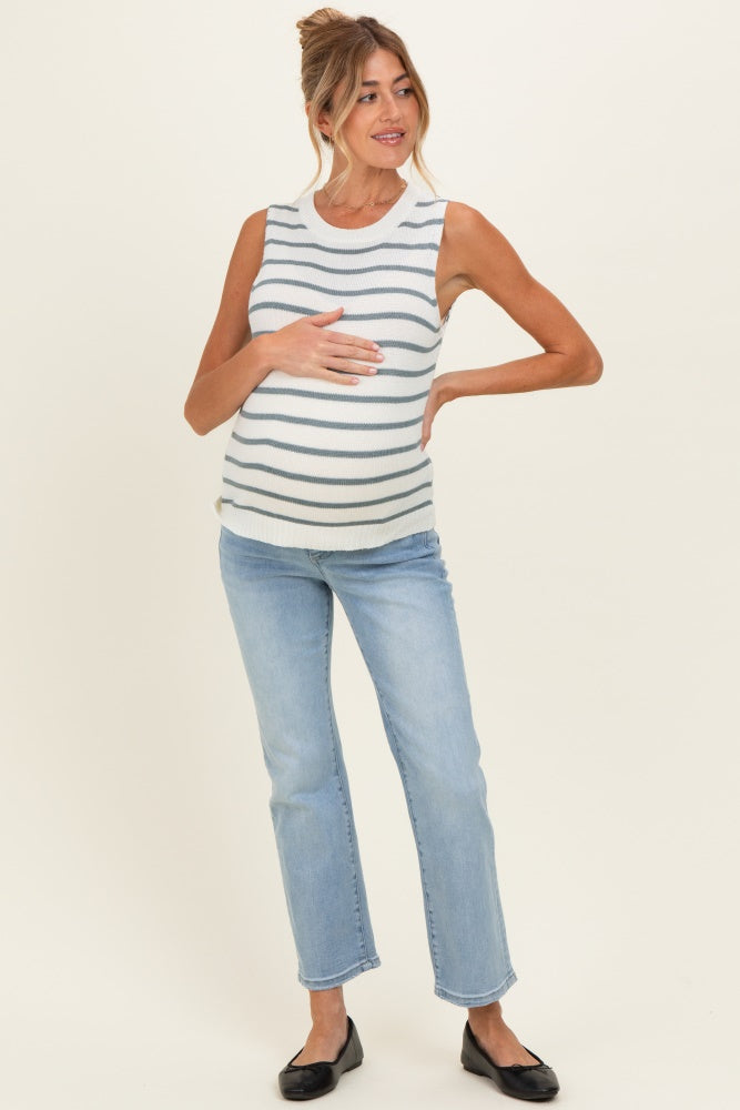 woman wearing a striped maternity tank top and light blue jeans, cradling her baby bump