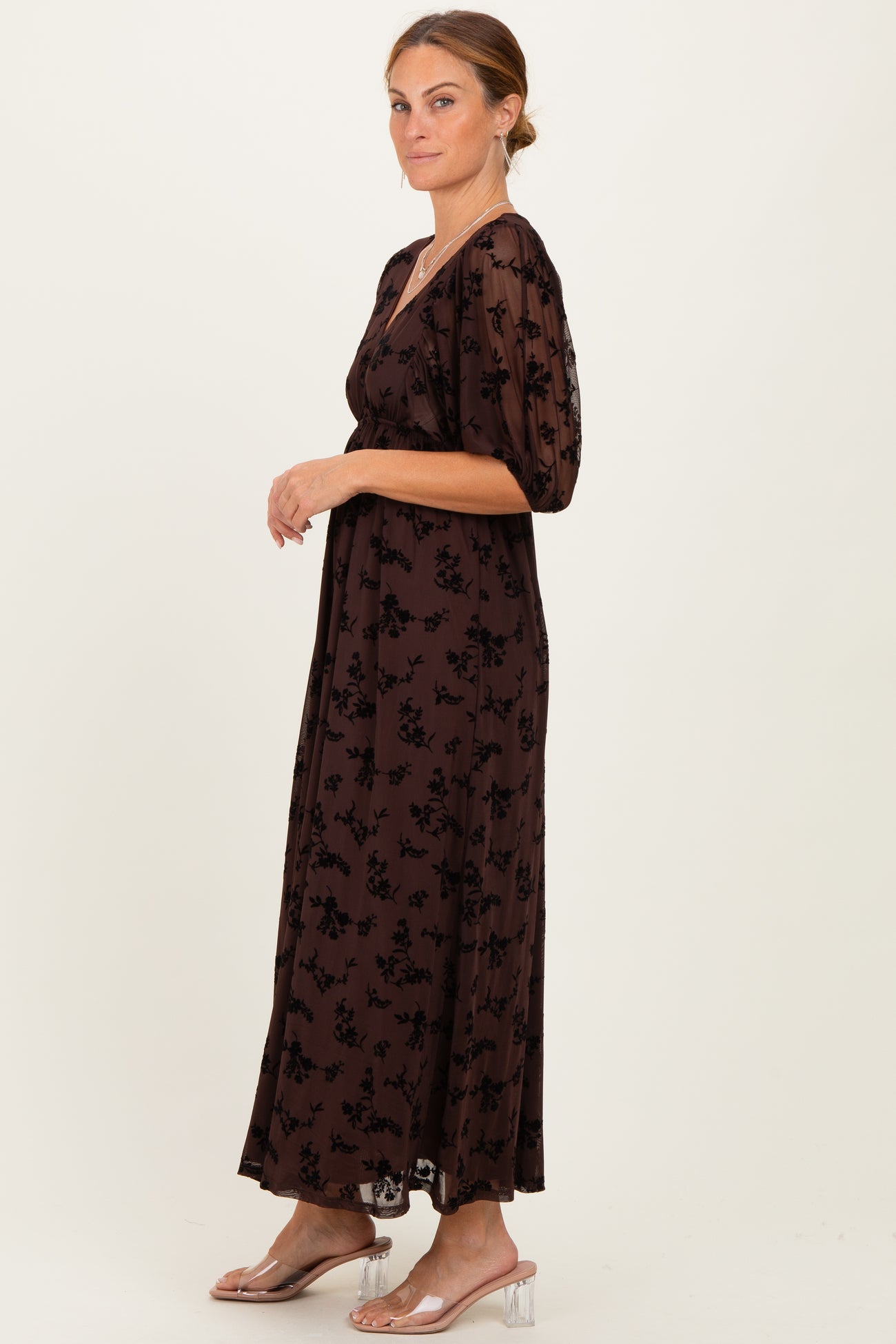woman wearing a brown floral maxi dress with puff sleeves and a cinched waist, standing profile on a light background