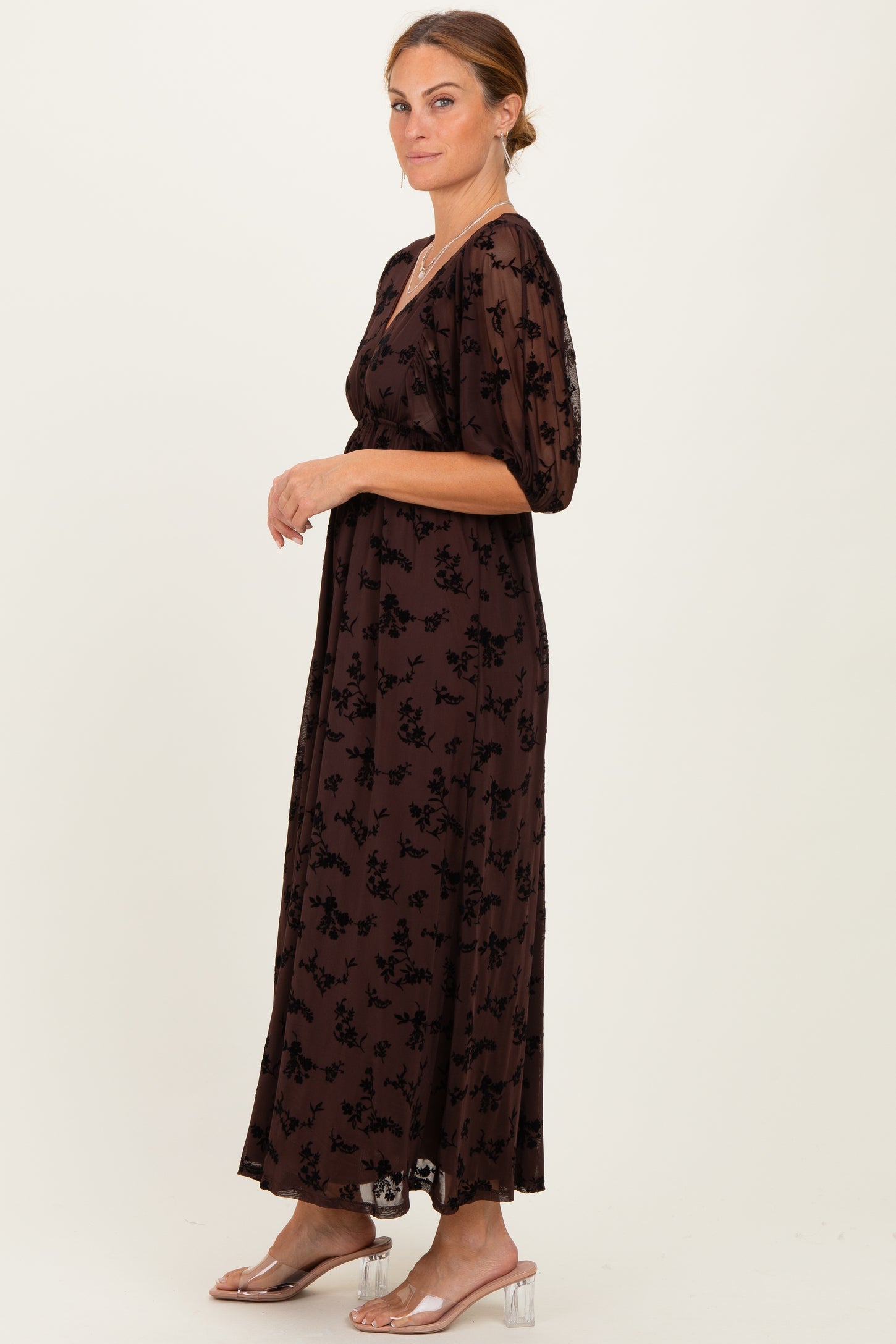 woman wearing a brown floral maxi dress with puff sleeves and a cinched waist, standing profile on a light background