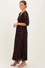 woman wearing a brown floral maxi dress with puff sleeves and a cinched waist, standing profile on a light background