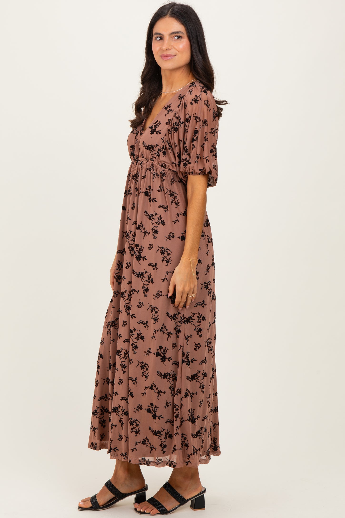 woman wearing a brown floral print maxi dress with puff sleeves and a fitted bodice, standing sideways