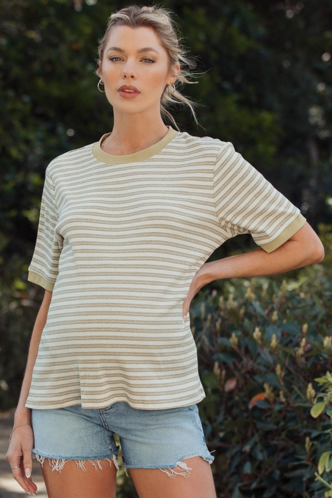 woman wearing a striped beige and white maternity top with green trim and denim shorts, showing a baby bump