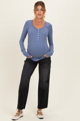 woman wearing a blue ribbed maternity top with buttons and holding her baby bump, paired with black wide-leg jeans