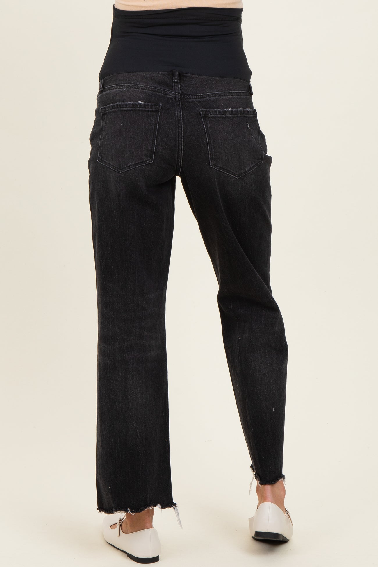 woman wearing black maternity jeans with a high waist and distressed hem, showing the back view