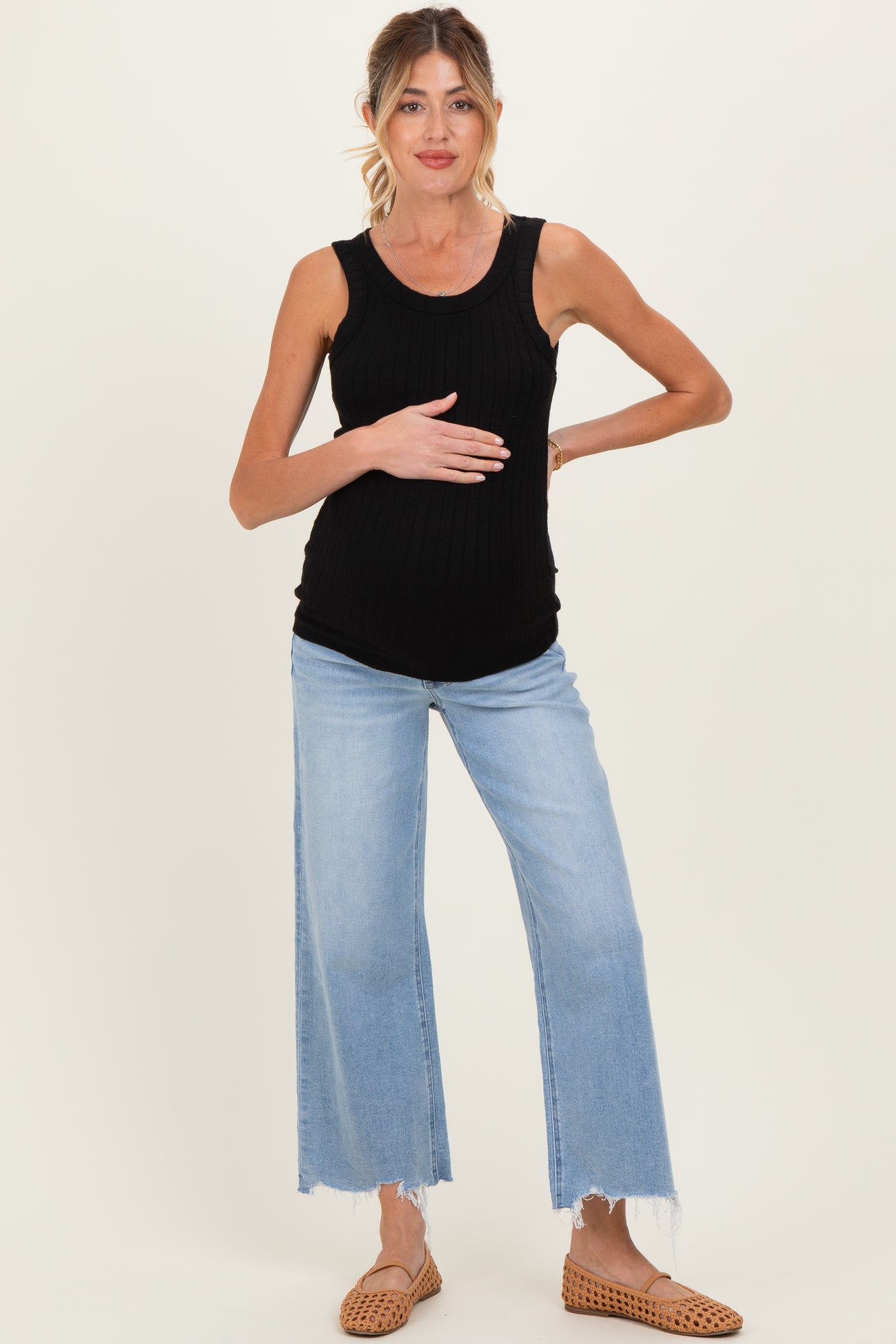 woman wearing a black ribbed maternity tank top and light blue wide-leg jeans, holding her baby bump