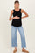 woman wearing a black ribbed maternity tank top and light blue wide-leg jeans, holding her baby bump