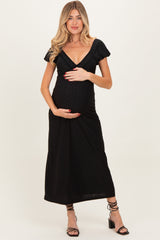 woman wearing a black maternity dress with short puff sleeves and holding her baby bump