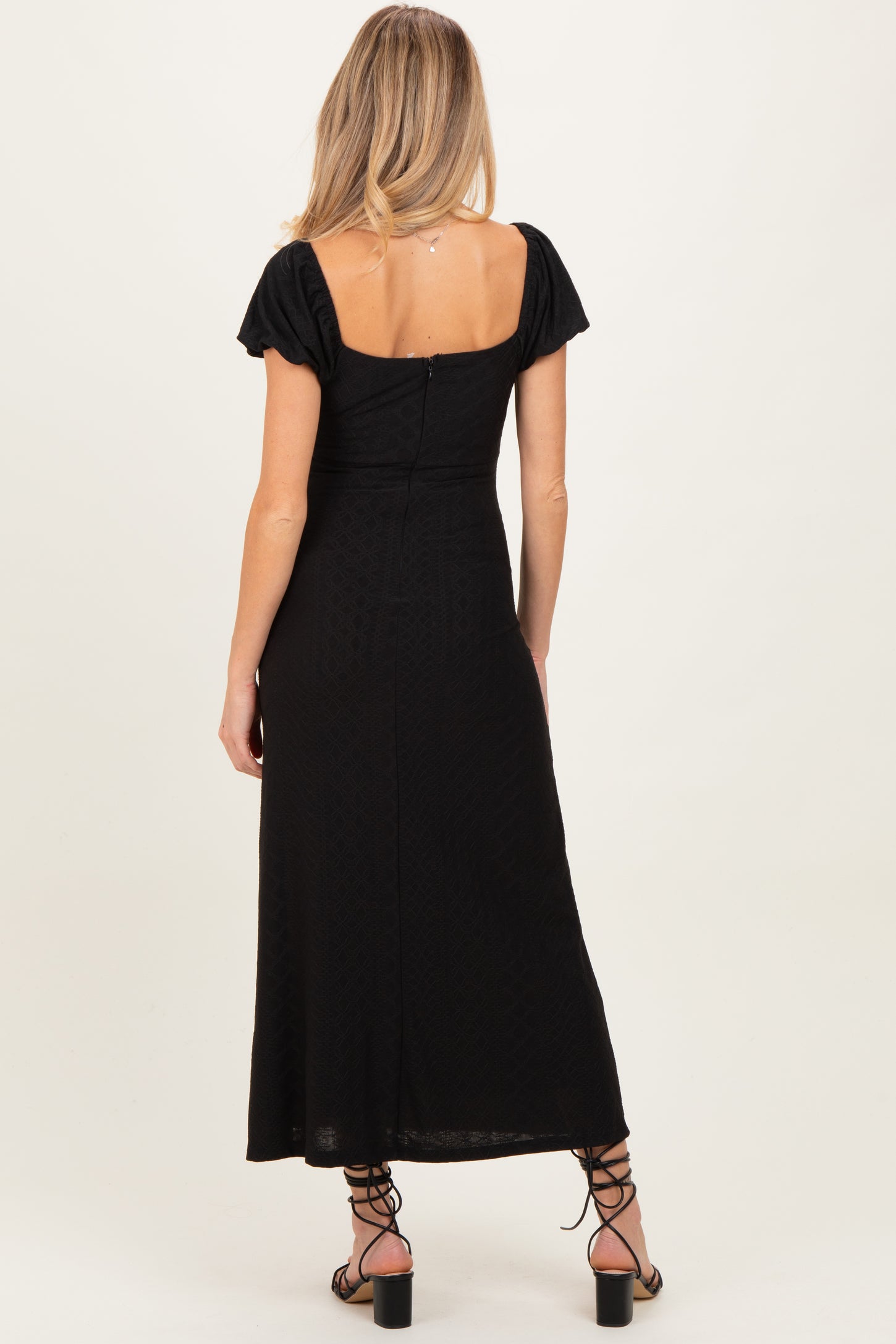 woman wearing a black maternity maxi dress with short puff sleeves and a low back.
