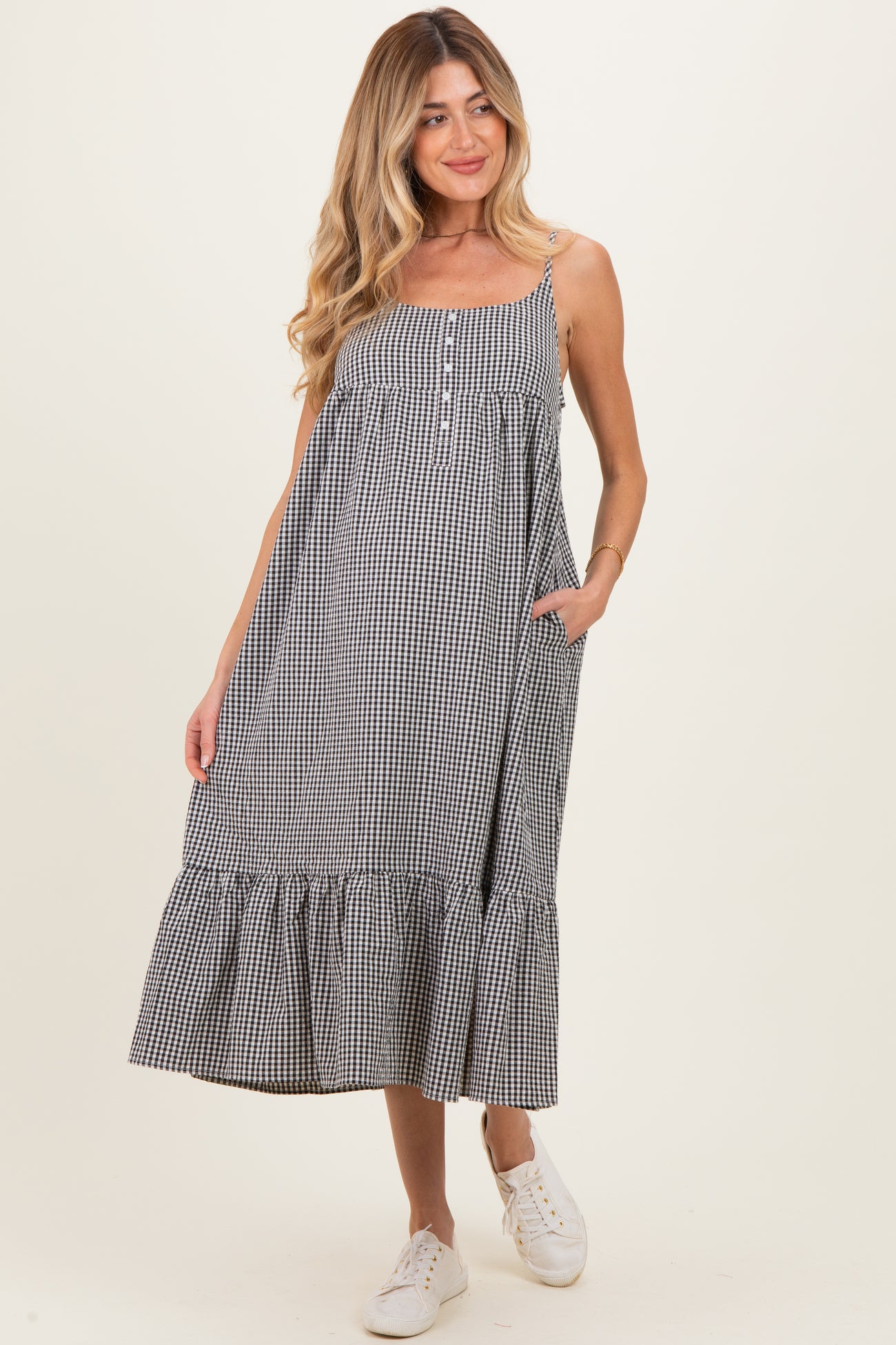 woman wearing a black and white gingham maternity dress with a button detail and ruffled hem, smiling and standing with hands in pockets