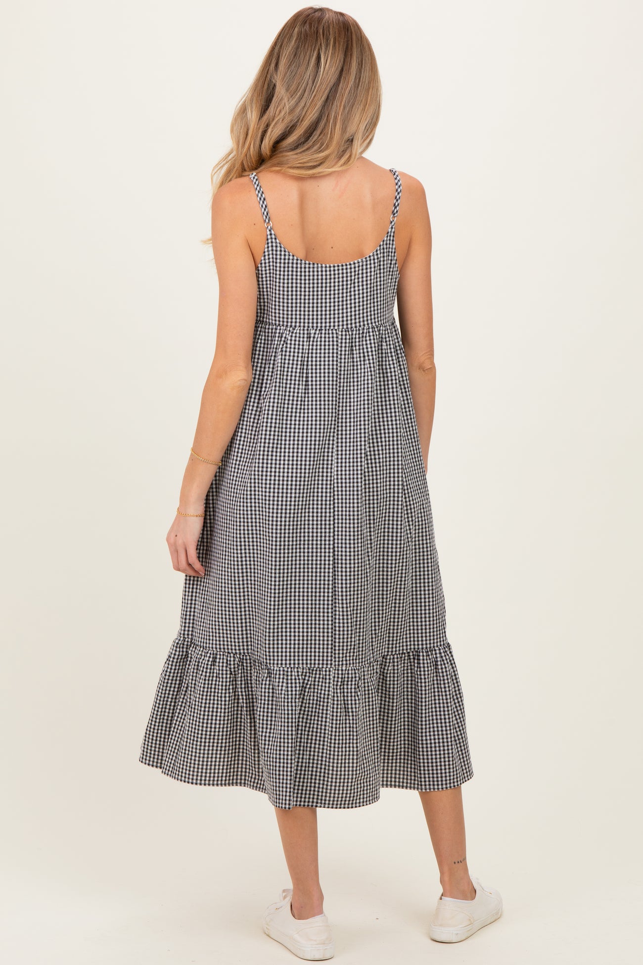 woman wearing a black and white gingham maternity dress with a ruffled hem and adjustable straps, showing off her baby bump