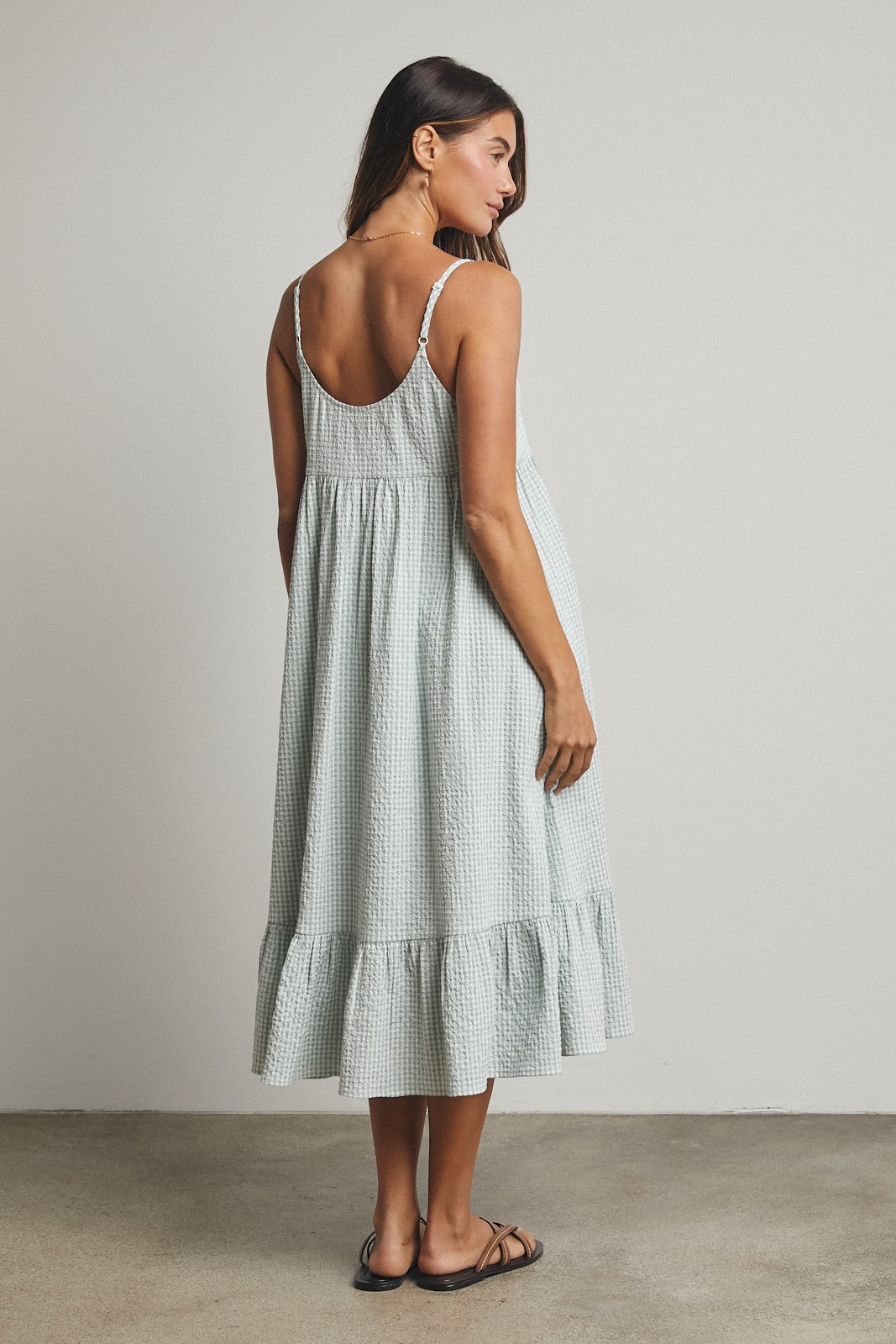 woman wearing a light green checkered midi dress with a flounced hem and spaghetti straps, viewed from the back