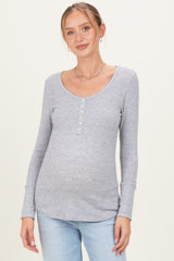 woman wearing a light gray long sleeve maternity top with a scoop neckline and button details, showing a baby bump