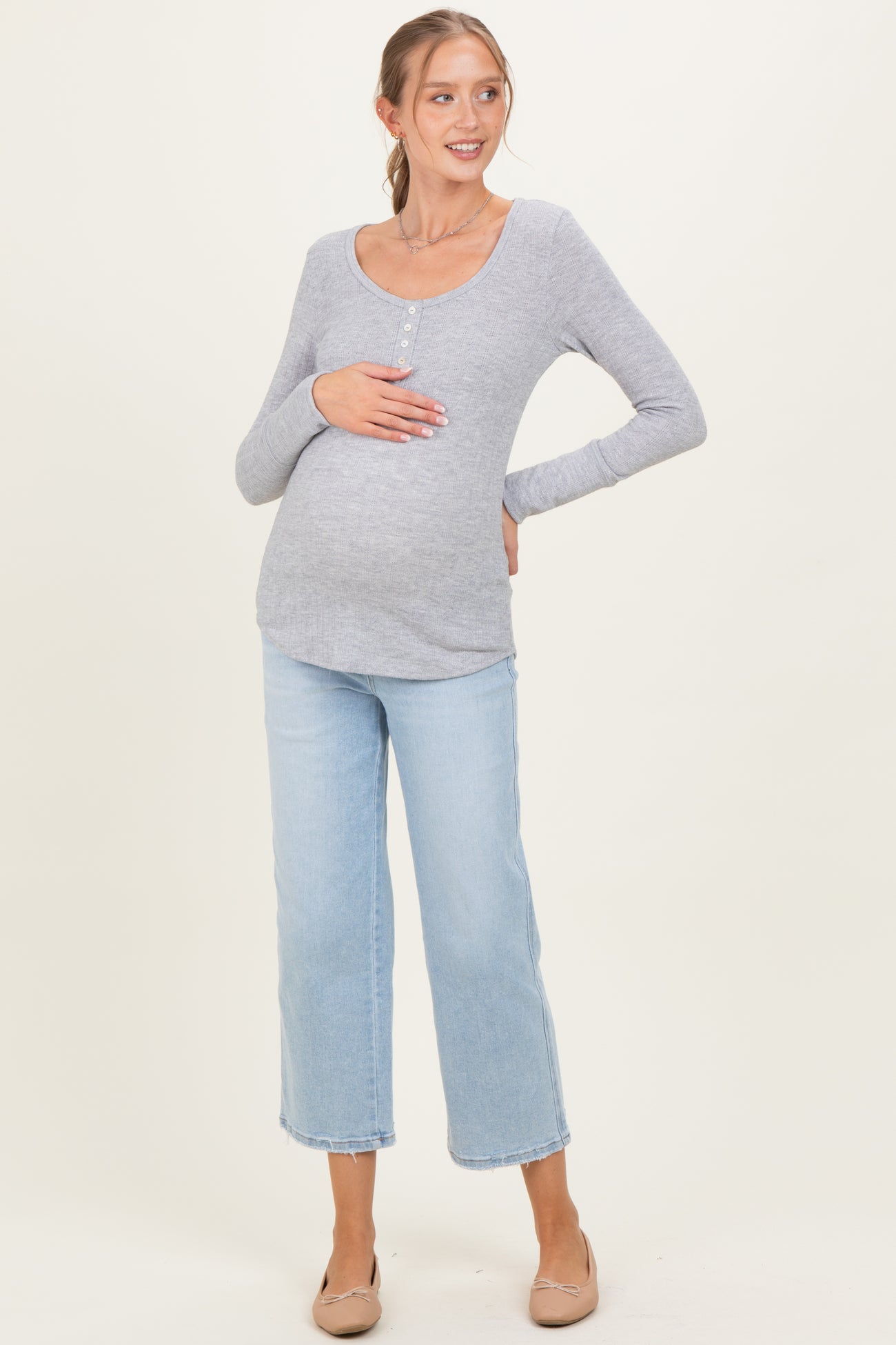 woman wearing a gray long sleeve maternity top and light blue cropped jeans, showing her baby bump