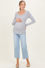 woman wearing a gray long sleeve maternity top and light blue cropped jeans, showing her baby bump