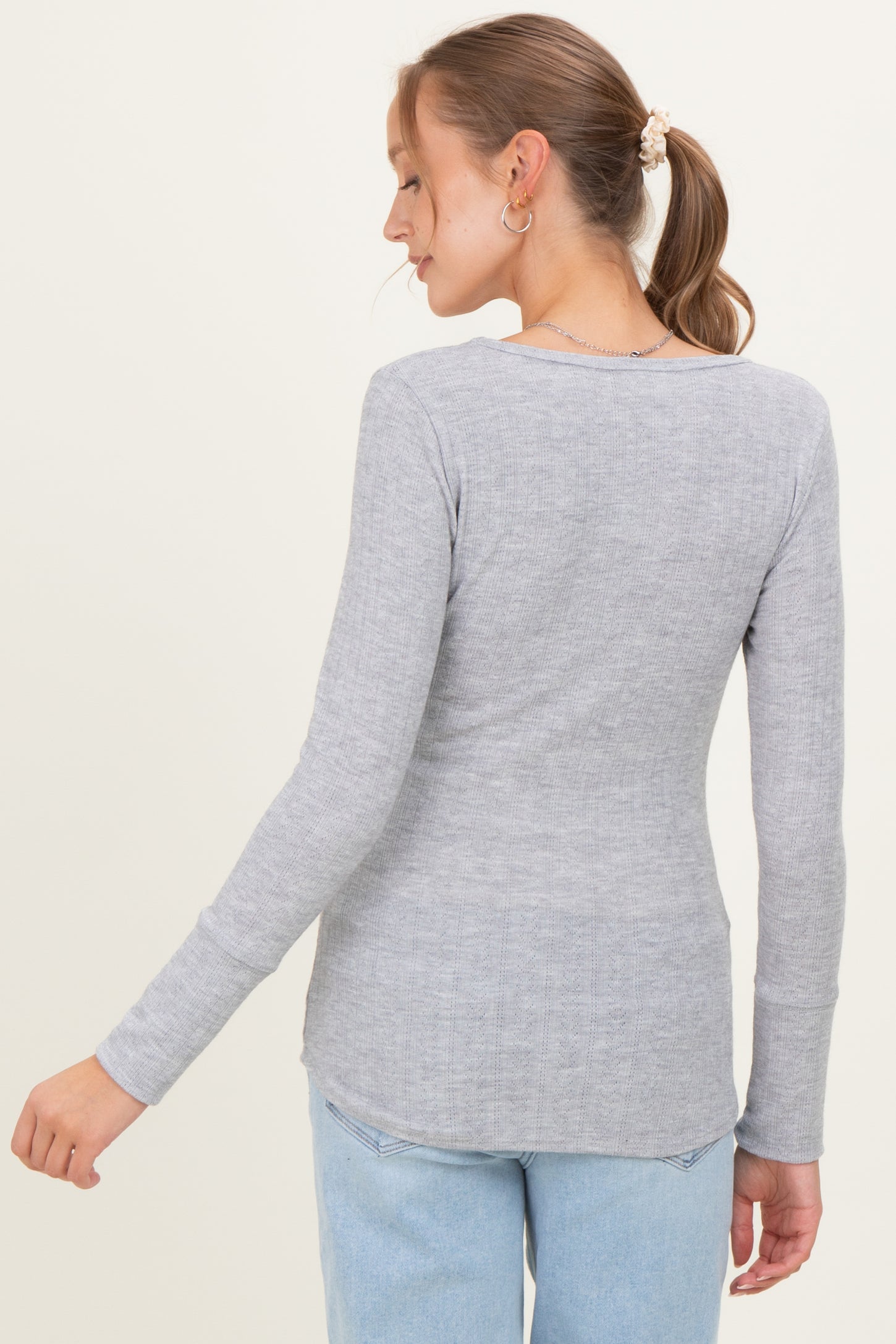 woman wearing a light grey long sleeve maternity top with a fitted style and rounded hem