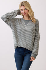 woman wearing a gray and white striped long sleeve sweatshirt with a relaxed fit and a v-neckline, paired with blue jeans