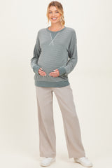 woman wearing a striped green maternity sweatshirt and beige wide leg pants while holding her baby bump