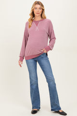 woman wearing a striped burgundy and pink maternity sweatshirt with long sleeves and holding her baby bump, paired with flared jeans