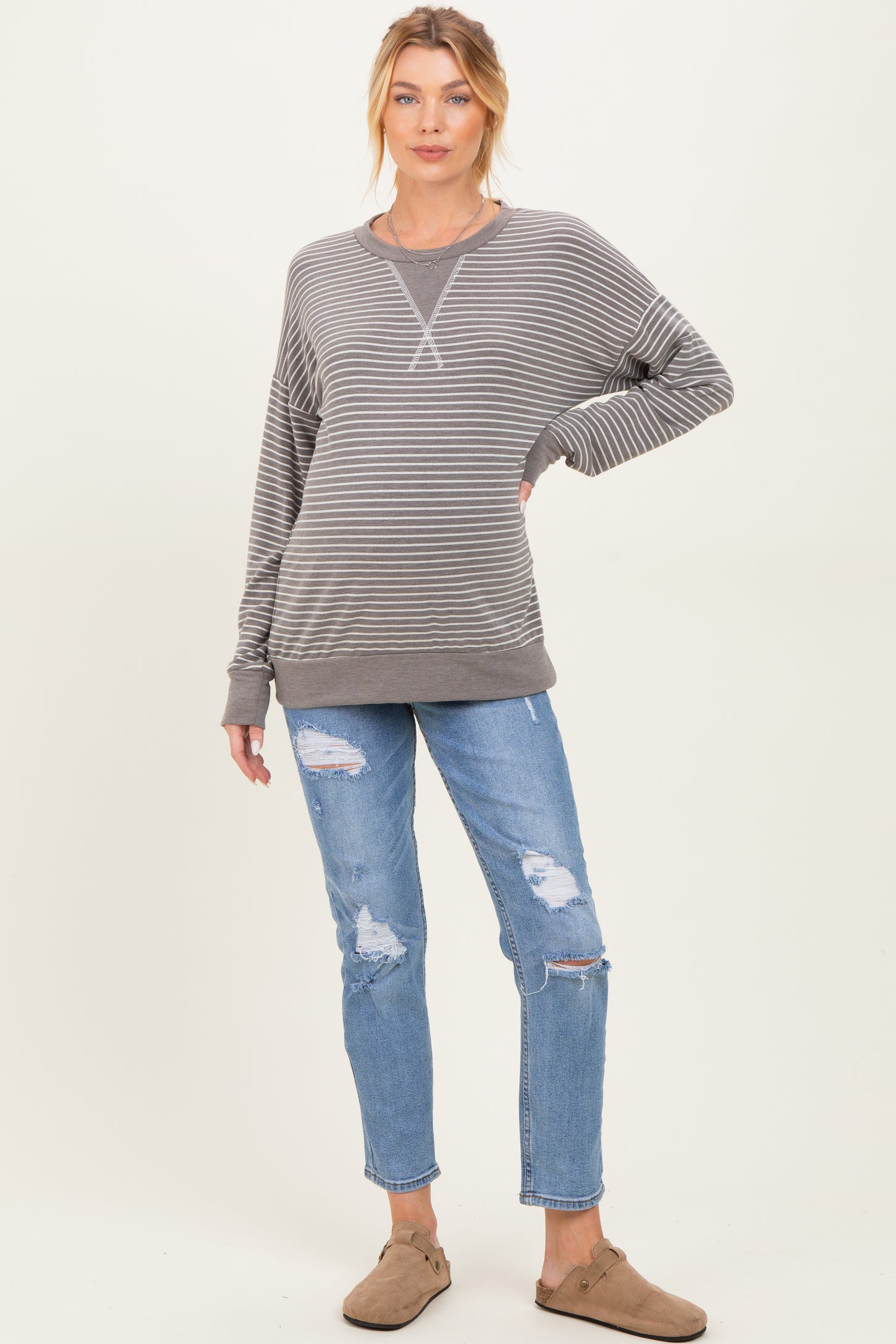 woman wearing a gray striped maternity sweatshirt with a relaxed fit and blue ripped maternity jeans, showcasing a baby bump