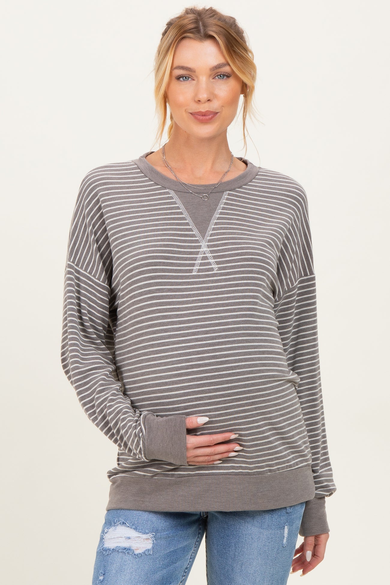 woman wearing a gray striped maternity sweatshirt and holding her baby bump