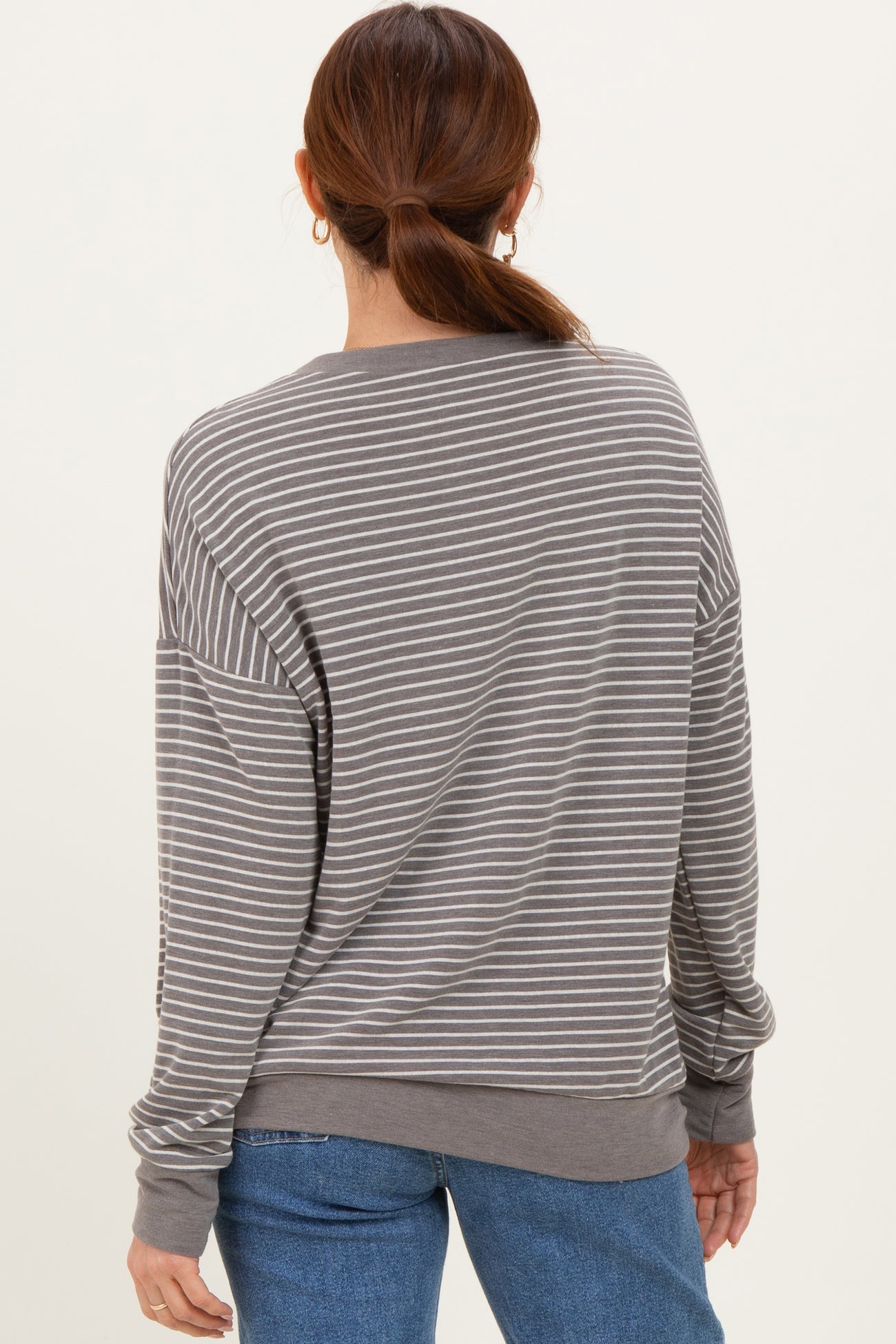 woman wearing a gray and white striped long sleeve oversized sweatshirt, viewed from the back