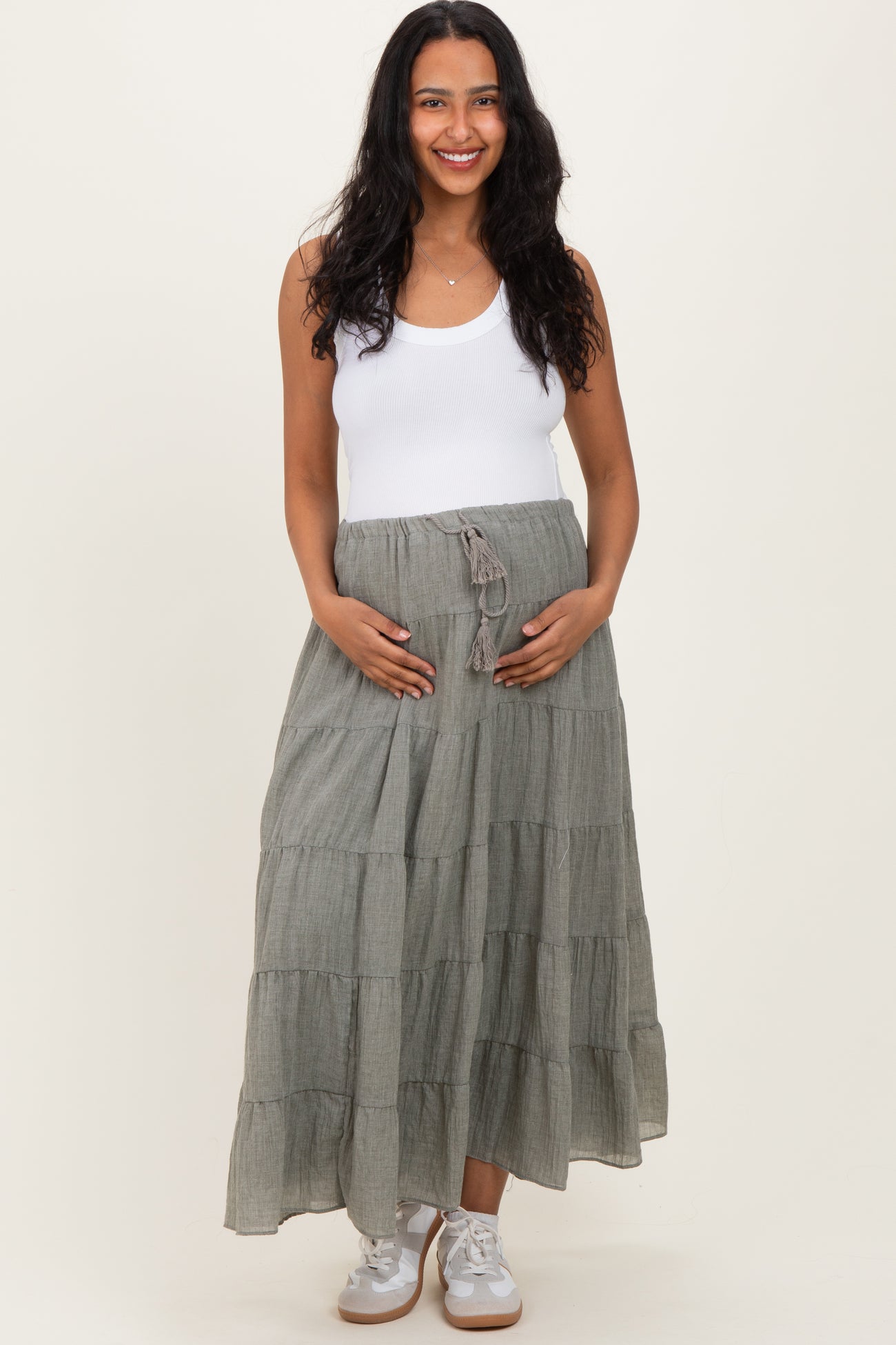 woman wearing a white tank top and a long gray tiered maternity skirt, holding her baby bump