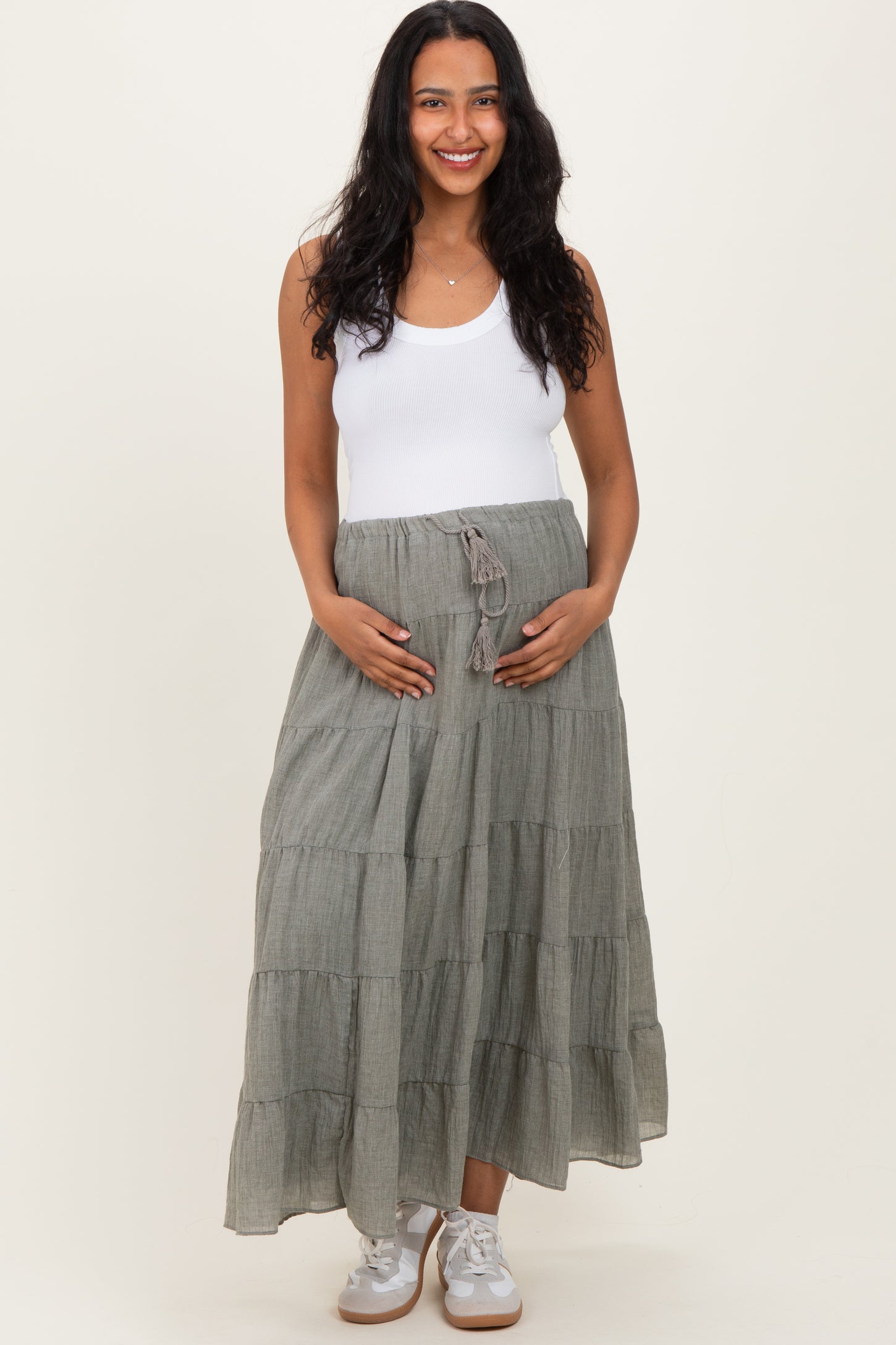 woman wearing a white tank top and a long gray tiered maternity skirt, holding her baby bump