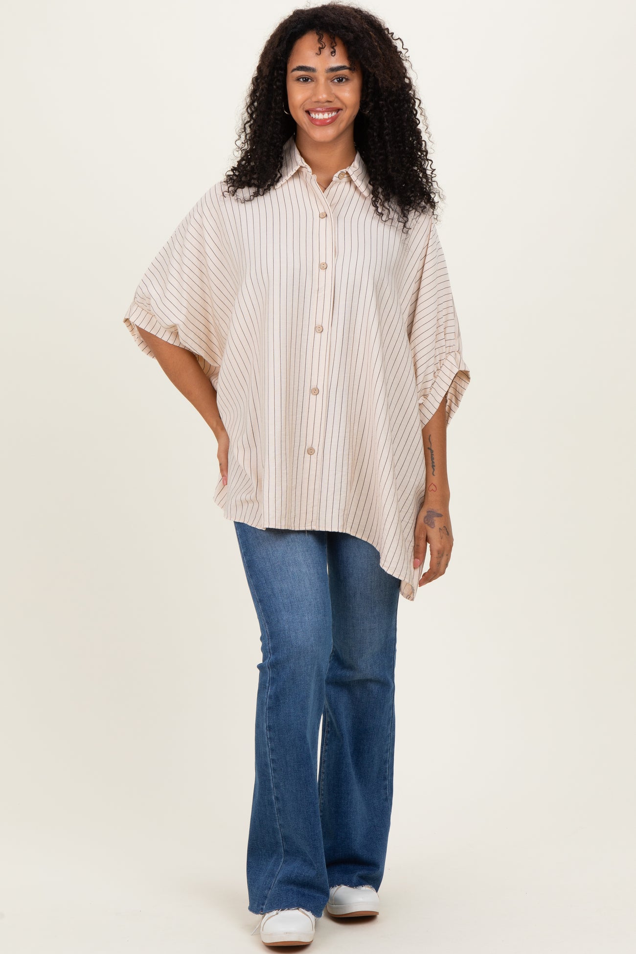woman wearing a beige striped oversized button-up shirt with rolled sleeves and blue flared jeans