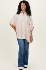 woman wearing a beige striped oversized button-up shirt with rolled sleeves and blue flared jeans